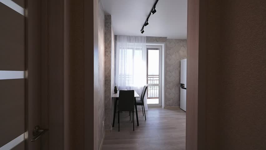 Modern compact kitchen with white cabinetry, sleek countertop, black sink, textured light-gray walls, minimalist design, doorway leading to another room, dark chair visible.