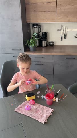 Little girl decorating Easter eggs with colorful stickers while sitting at table at home. Creative Easter activity, simple egg decoration technique and joyful holiday preparation indoors