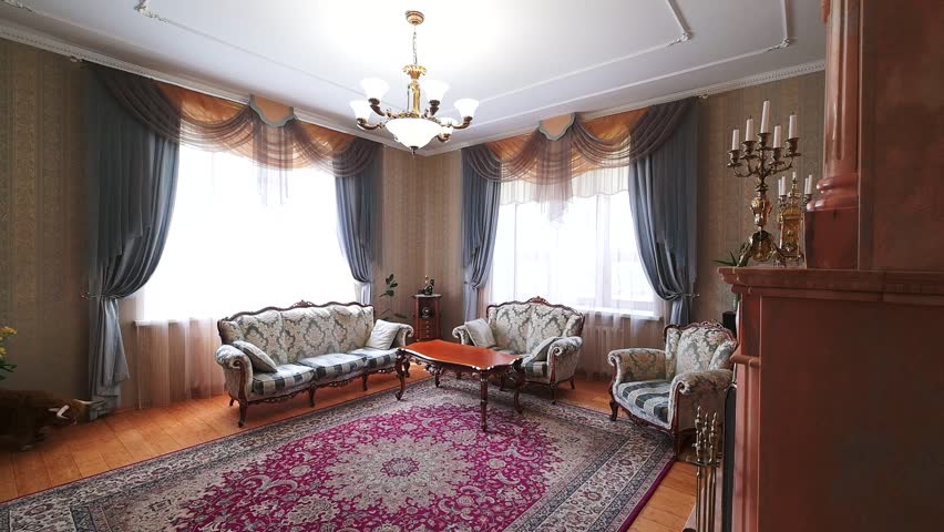 classic living room with two sofas, two armchairs, a wooden coffee table, patterned rug, heavy drapes, chandelier, warm wooden flooring, light walls.