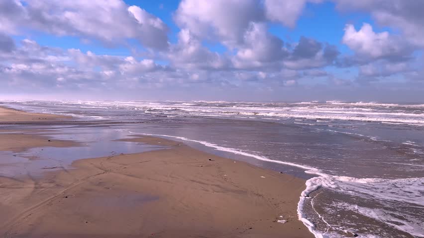 Seaside scene of open sandy beach under blue sky with clouds and waves