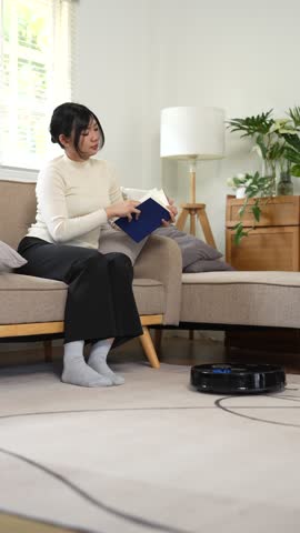 Robotic vacuum cleaner cleaning the room while woman resting on sofa.