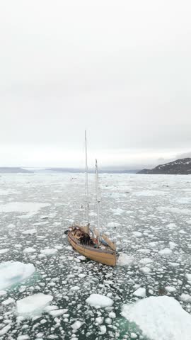Sailing yacht navigates Arctic sea filled with icebergs near Greenland coast