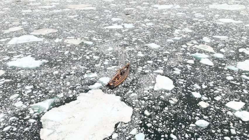 Sailing yacht remains motionless among Arctic icebergs near Greenland coastline