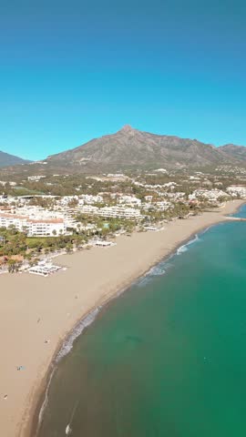 Vertical aerial view of Marbella beach, Costa del Sol, Southern Spain, with iconic La Concha mountain in the background on a bright Mediterranean day.
