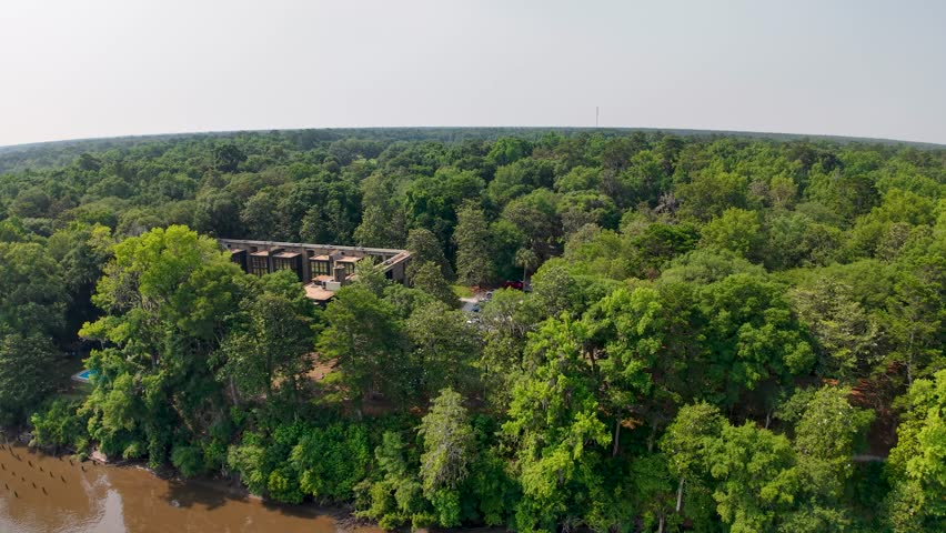 Drone footage provides an aerial view of a tree-covered plantation landscape with brown-roofed buildings and green fields at Middleton Place Plantation near Charleston, South Carolina.