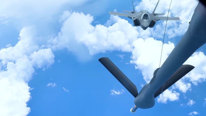 Fighter jet conducting aerial refueling with tanker plane under clear blue sky and clouds.