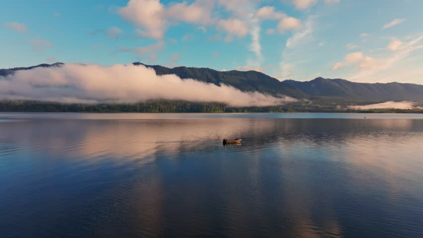 Aerial drone view of Lake Quinault at golden hour, capturing calm water, warm sunrise light, and surrounding rainforest in Olympic National Park. Ideal for nature and landscape footage.