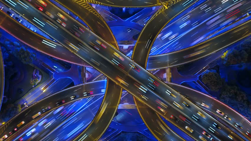Aerial top down time lapse view of complex highway interchange at night. Busy traffic with light trails on modern road infrastructure. Futuristic transportation and logistics concept