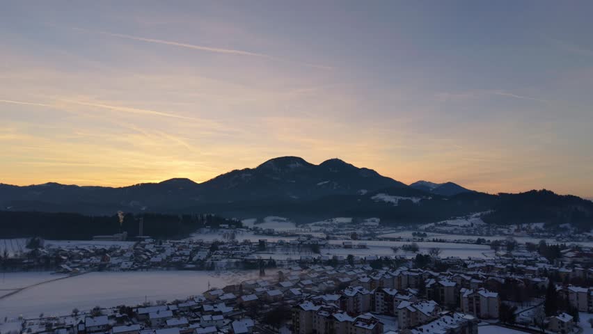 Snowy winter landscape with orange sunset behind mountains