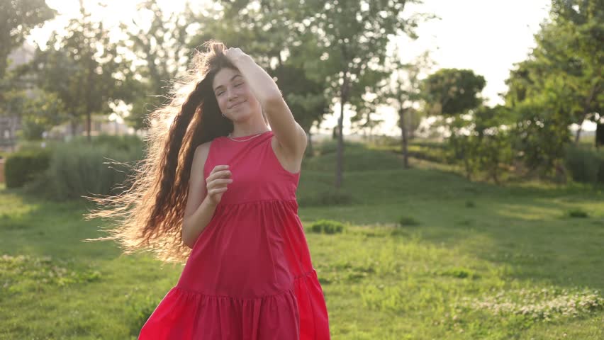 a beautiful teenage brunette girl with long hair, smiling, looking at the camera during a summer walk