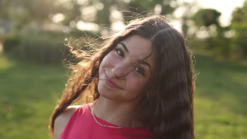 a beautiful teenage brunette girl with long hair, smiling, looking at the camera during a summer walk