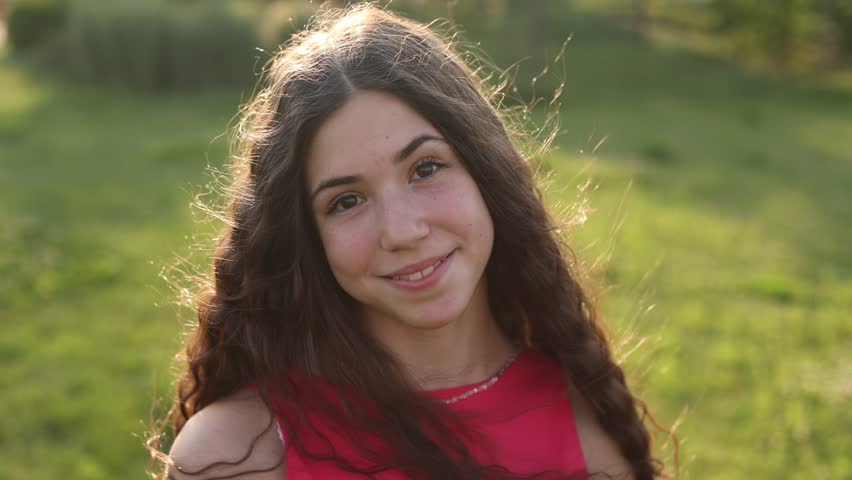 a beautiful teenage brunette girl with long hair, smiling, looking at the camera during a summer walk