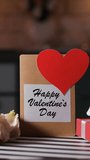 Vertical video. Rose petals fall onto a table with a bouquet a Valentines card and a gift box symbolizing love, slow motion - Powered by Shutterstock - Get 15% off with code: PIKWIZARD15