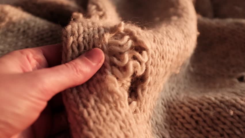 Closeup video of hands touching soft knitted wool sweater with a hole in it. Damaged torn knitted handmade sweater. Appreciating pleasant texture of high quality textile for clothes. Soft and cozy textile. Ivory winter knitted sweater. 