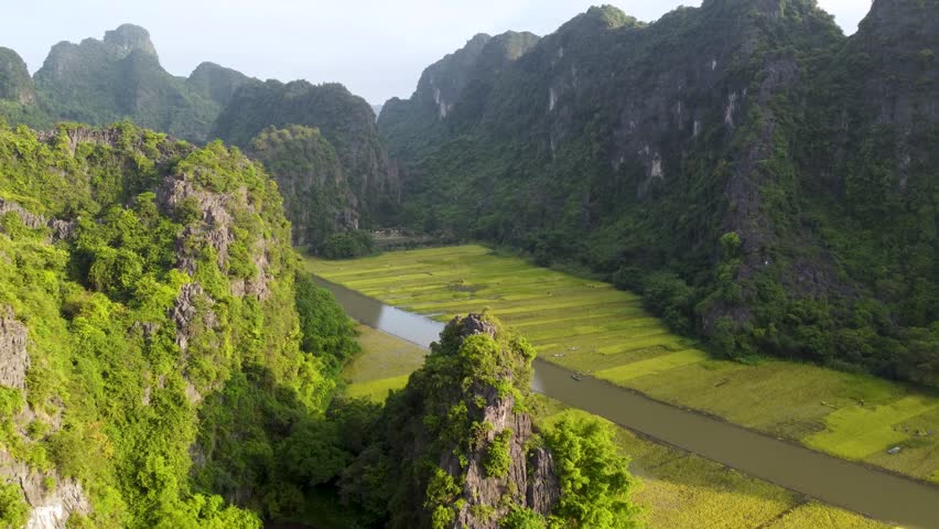 Drone aerial flyover across limestone karst hills and cultivated rice fields in Ninh Binh, Vietnam.