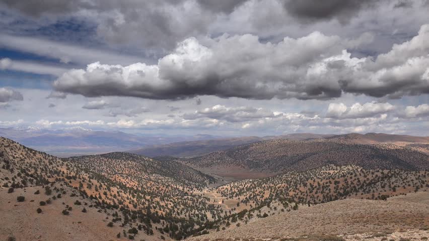 Time lapse cloudscape over arid Atlas Mountains with sparse trees under Mediterranean climate. Dramatic light moves across rugged ridges in North Africa showing semi arid mountain landscape.