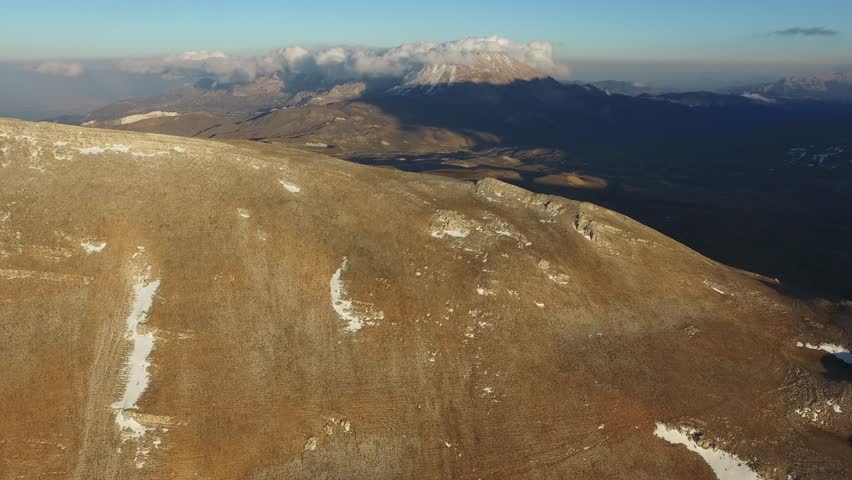 Aerial panoramic view of high altitude plateaus surrounding rugged mountain ranges. Wide landscape perspective shows vast terrain, peaks, ridges, valleys, and natural geology.