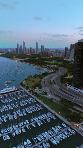 Drone perspective shows organized marina slips, moored boats, sweeping lakeshore highway and distant skyscrapers under soft morning light creating calm coastal urban depth