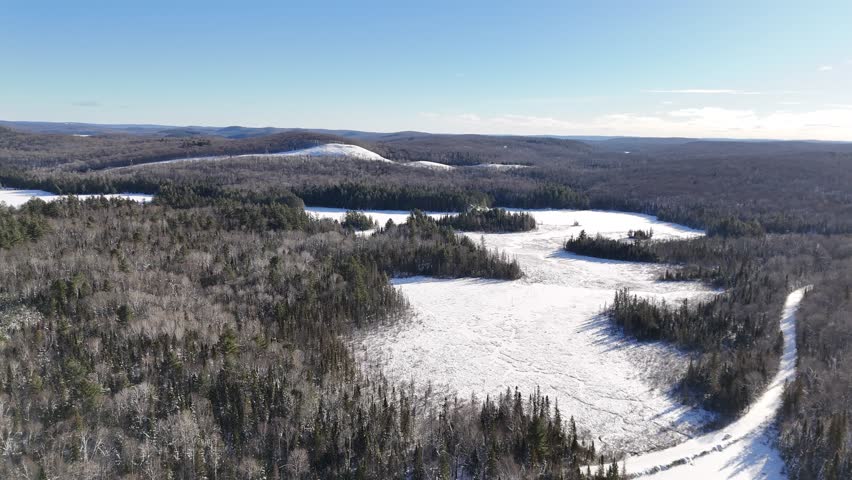 Bright, sunny aerial view of a snowy forest surrounding two partially frozen Oram Lake in Algonquin Provincial Park