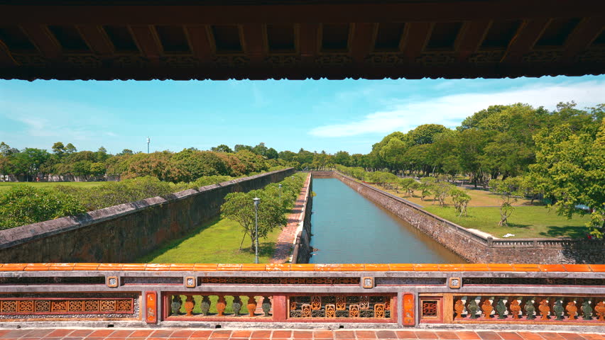 A perfectly framed shot from the upper level of the Noon Gate (Ngo Mon), looking down at the straight line of the protective moat, stone walls, and lush green gardens of the Citadel.
