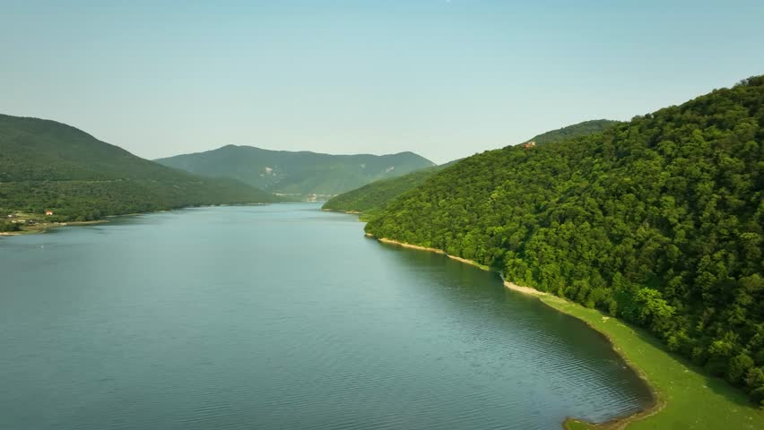 Aerial panoramic view of a wide mountain lake in Georgia, framed by lush green hills and smooth calm water.