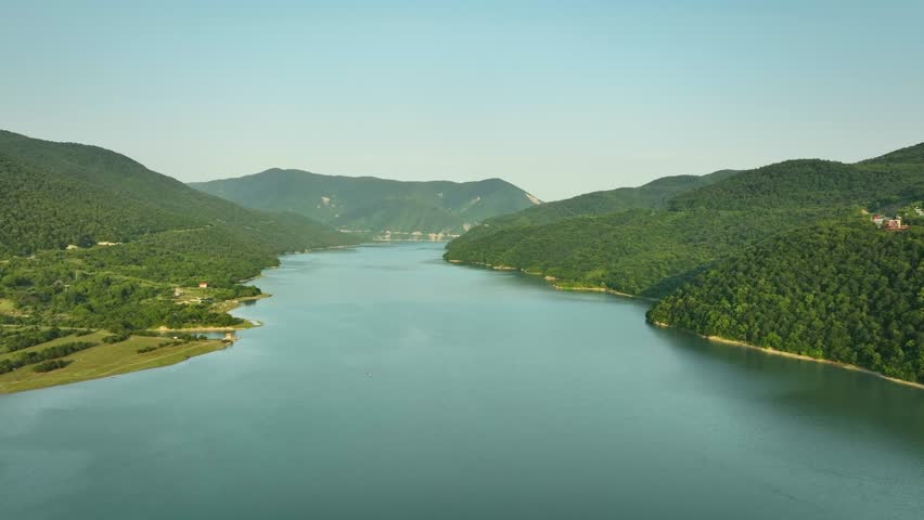 Aerial panoramic view of a wide mountain lake surrounded by green forested hills in Georgia, showcasing calm water and untouched nature.