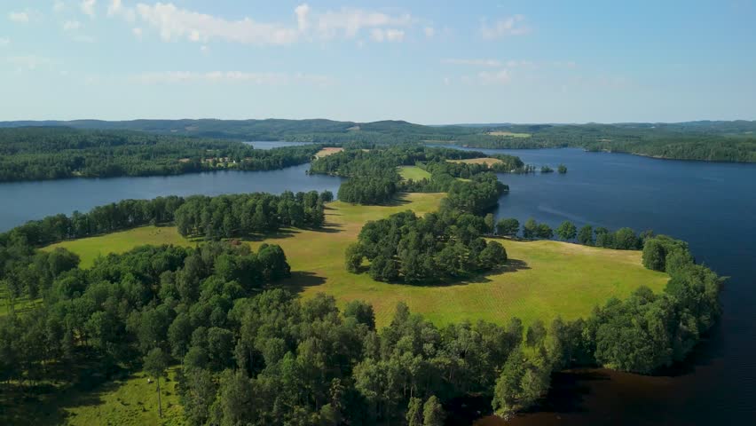 Aerial flying forward above Baldersnäs Herrgård peninsula surrounded by calm lakes forests and open green fields in Swedish countryside