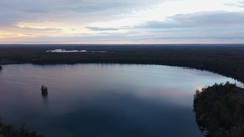Aerial of calm river bordered by forest at sunset near rural Peterborough Ontario Canada