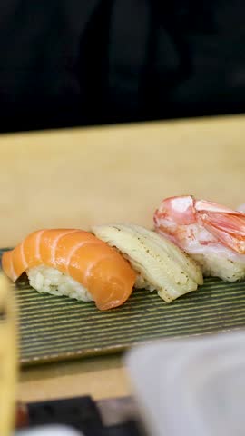 Close-up shot of salmon, white fish, and shrimp nigiri sushi on a green plate.