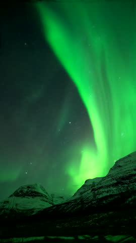 Northern lights ripple across dark sky above Tamokdalen valley in Tromso Norway, snowcapped mountain with starry sky, vertical