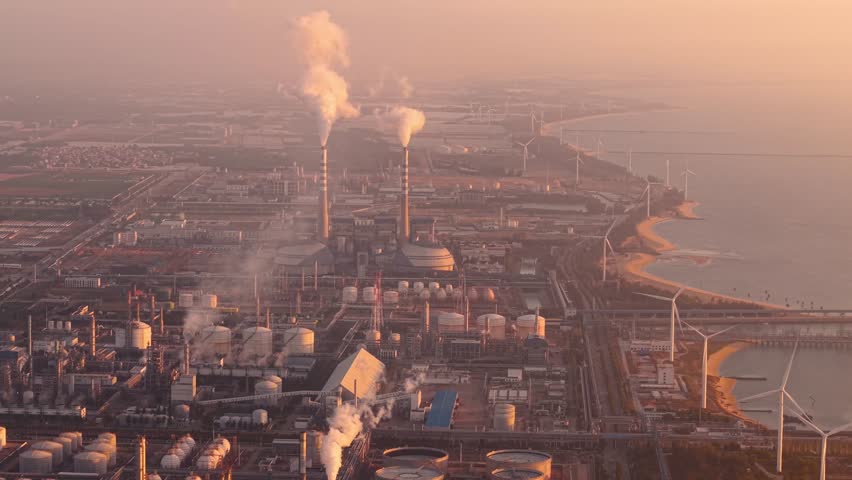 Industrial landscape chemical oil plant at sunset: smoke rising over coastal factory.