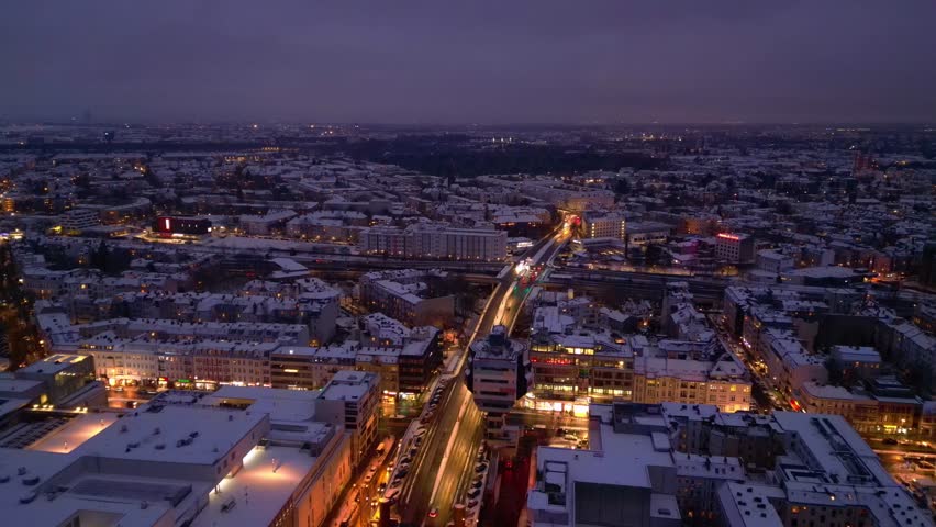 urban shopping street architecture and illuminated streets of Berlin Steglitz district covered in fresh snow during snowy winter evening. Beautiful aerial view fly push forward overflight flyover dr