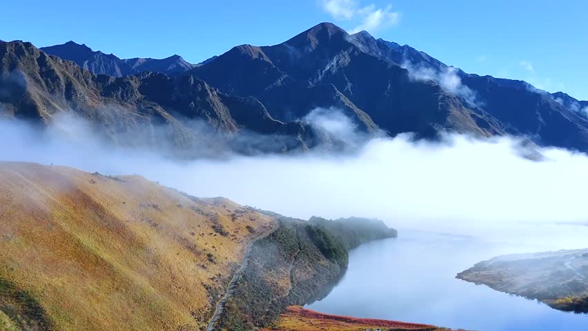 Stunning aerial perspective of low-lying clouds over a peaceful lake surrounded by rugged mountain peaks.