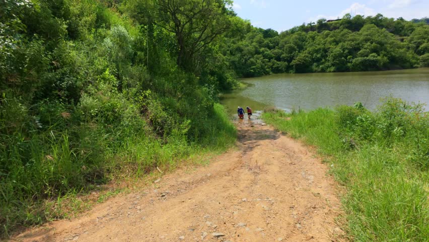 Two Hikers On Dirt Trail Walking Away From Calm Lake Near El Carrizo Dam In Jalisco, Mexico. wide static shot