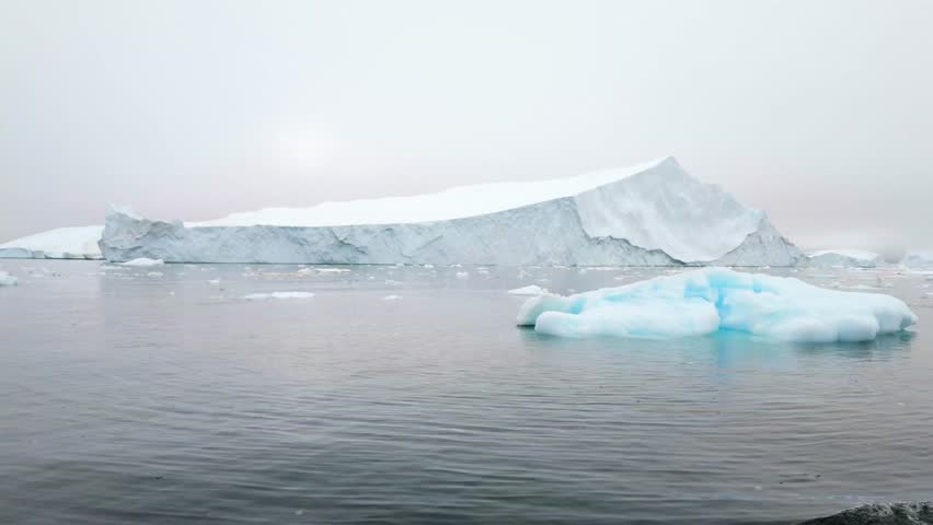 Sailing boat wake collides gently with small iceberg in Arctic fog in Greenland