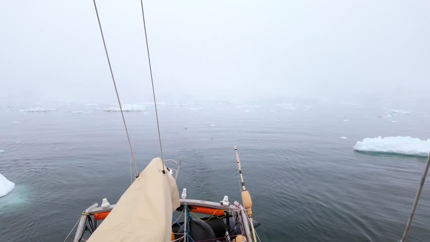 Rear view of sailing boat leaving icebergs behind in dense Arctic fog near Ilulissat