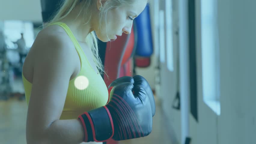 Animation of connected icons over caucasian woman wearing gloves punching boxing. Digital composite, multiple exposure, fitness, active lifestyle, communication, sport and training concept.