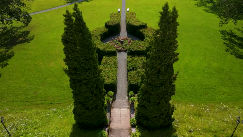 Drone camera tilts up to reveal symmetrical garden walkway with trimmed green bushes and perfectly manicured lawns at historic Baldersnas Herrgard manor estate in Dalsland Sweden