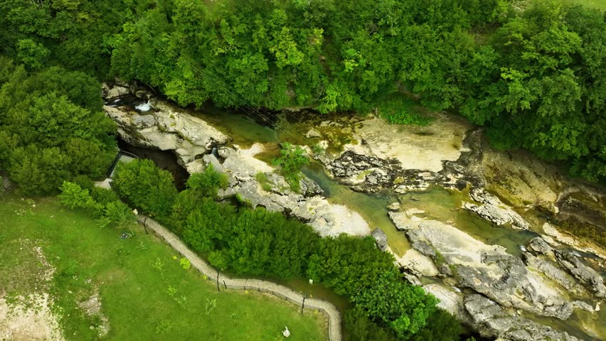 Aerial top-down view of a rocky river stream flowing through dense green forest in Georgia, showcasing untouched natural wilderness.