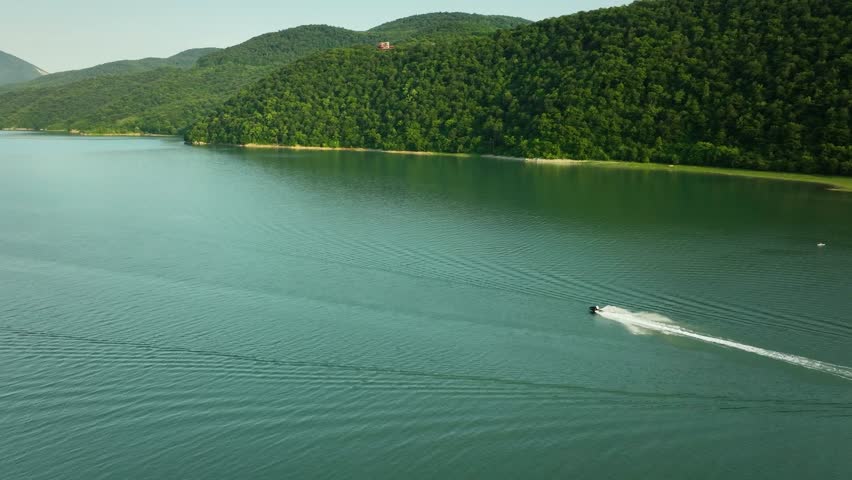 Aerial view of a speedboat leaving a wake across a mountain lake in Georgia, surrounded by green forested hills and open water.