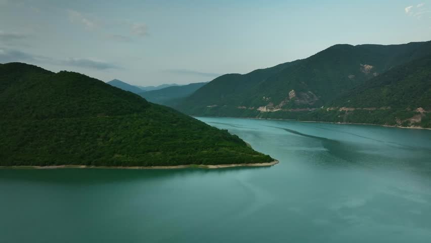 Aerial view of a green mountain peninsula extending into a calm lake in Georgia, surrounded by peaceful water and forested slopes.