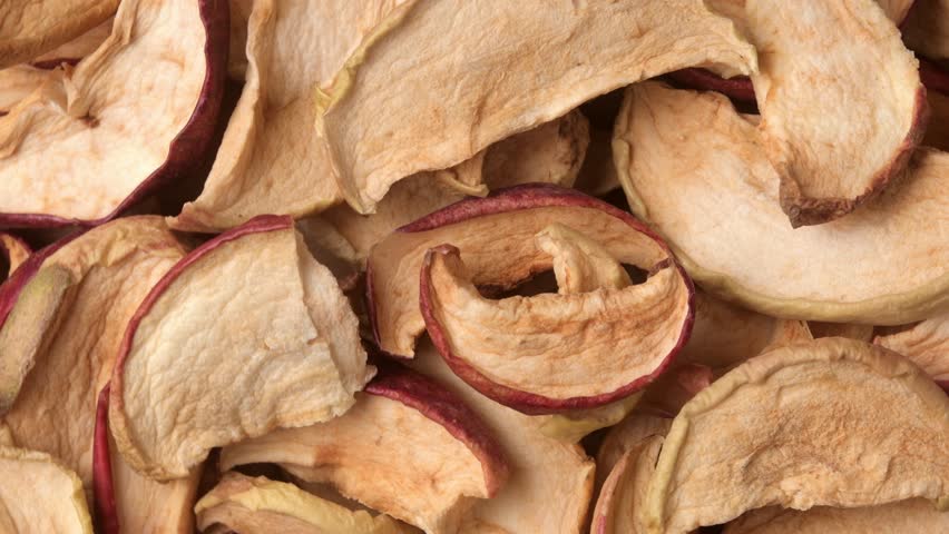 Rotating macro of dried apple slices and chips as natural snack texture background for healthy food, vegan dieting theme.