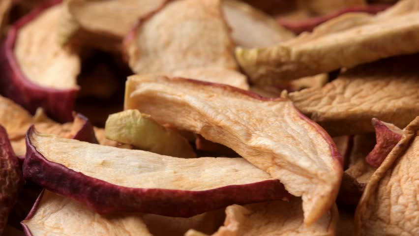Rotating close-up reveals dried apple slices with red peel as crunchy homemade snack texture background for healthy eating.