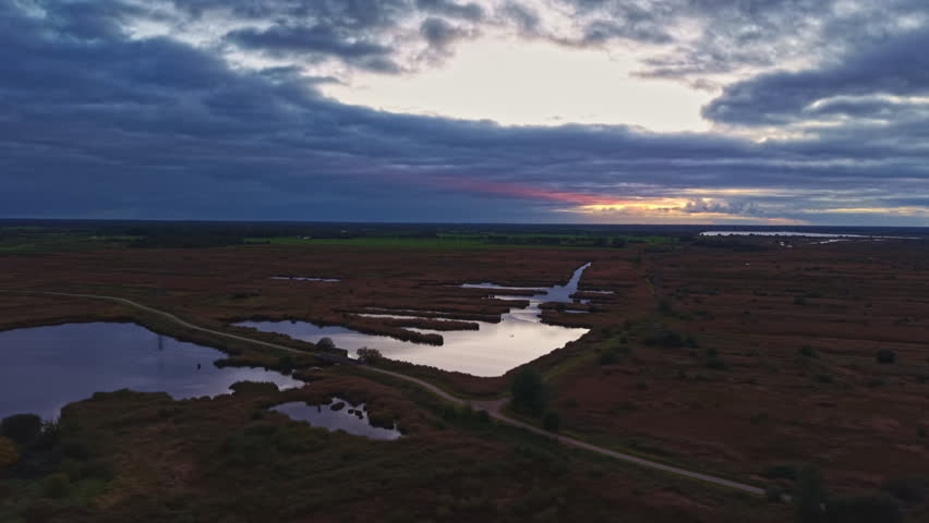 A beautiful sunset casts vibrant colors across marshlands, with still waters mirroring the sky. Soft light illuminates the scenery, creating a peaceful evening atmosphere.