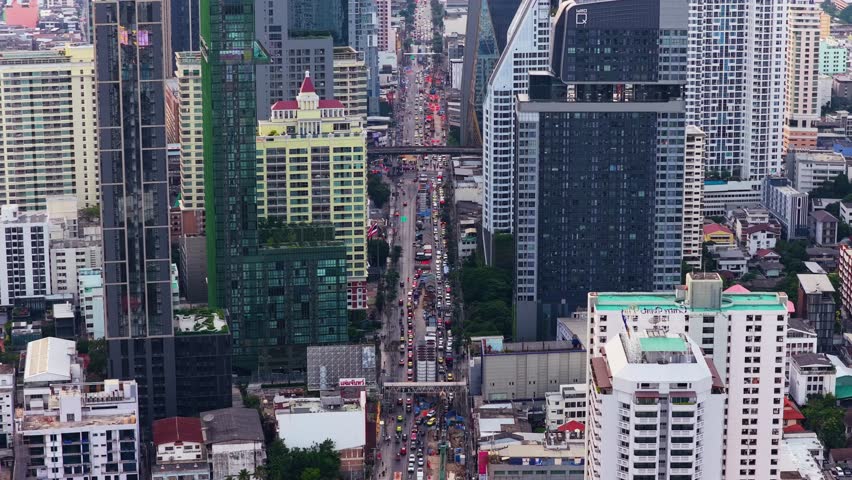 High angle tripod view of downtown Bangkok, Thailand, showing dense traffic moving along major road surrounded by modern urban architecture