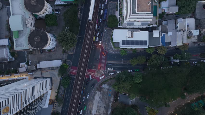 Aerial perspective following streets and railway line through Bangkok, Thailand. Modern buildings and a lush golf course flank the busy street traffic