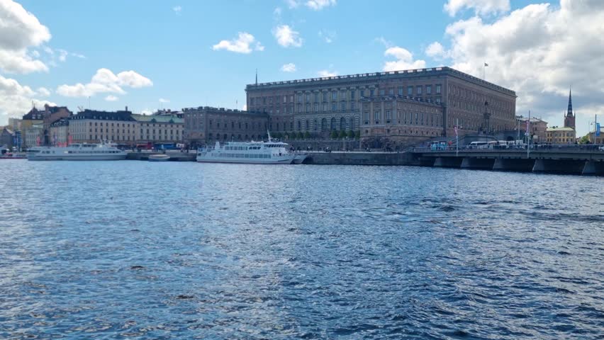 Waterfront view of Stockholm’s Royal Palace, Stockholms slott, seen across the Norrström under a bright blue sky, showcasing the city’s historic heart and royal architecture, Sweden