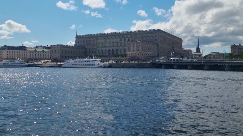 View of the Royal Palace (Stockholms slott) across Norrström in Stockholm, Sweden, under a clear blue sky, highlighting the historic waterfront and iconic royal architecture