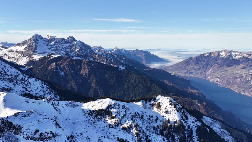 Churfirsten mountain range overlooking Walensee near Flumserberg, Switzerland with snow-covered alpine peaks, deep valley, clear sky and winter landscape view from aerial drone.