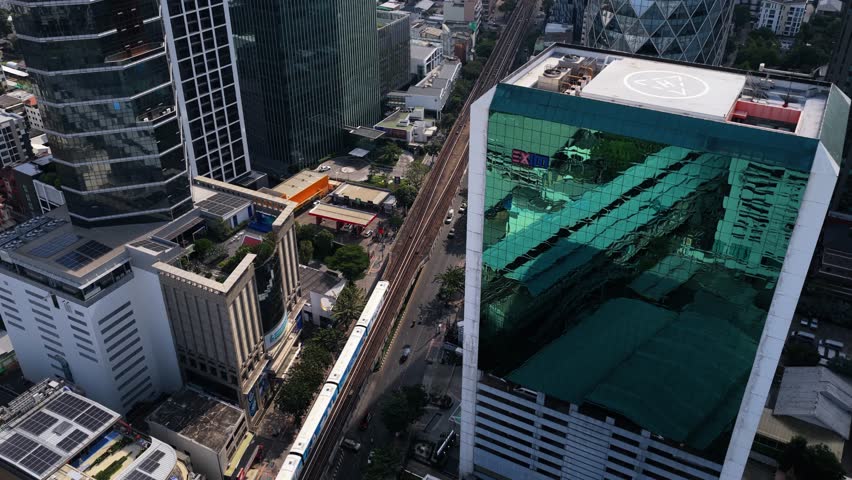 Elevated shot of a BTS Skytrain moving through Bangkok's urban landscape, passing modern skyscrapers and residential buildings